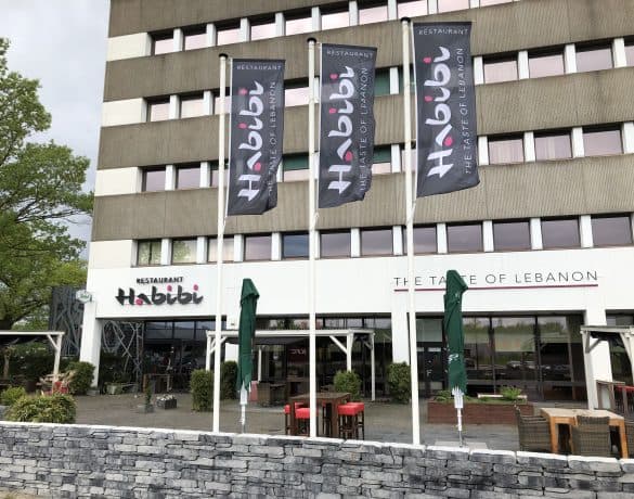 Vlaggen met het logo van Restaurant Habibi op masten voor de gevel